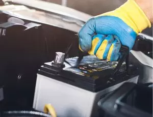A hand pulls a car battery out of an engine compartment