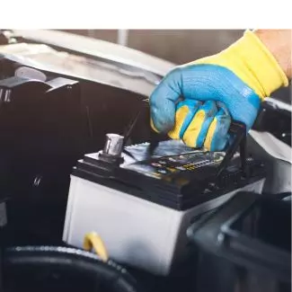 A hand pulls a car battery out of an engine compartment