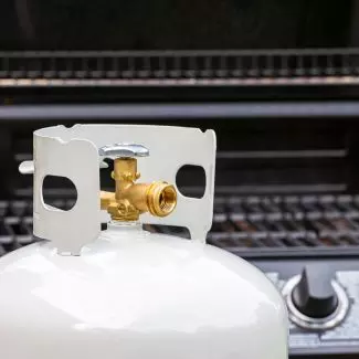 Propane tank in front of a backyard grill